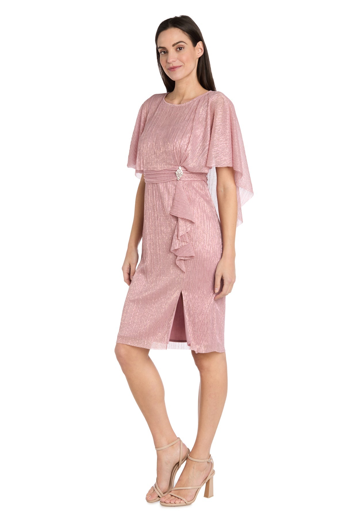 A woman models the R&M Richards 3195P caped knee-length party dress in shimmering pink with flutter sleeves and a waist detail, paired with nude heels, standing against a white background.